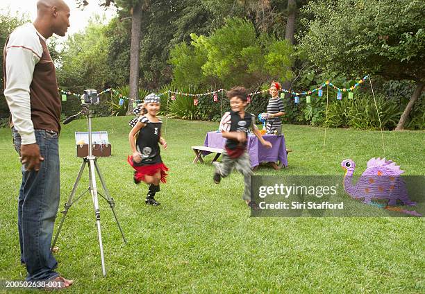 father videotaping children (7-10) playing in yard - memorial garden stock pictures, royalty-free photos & images