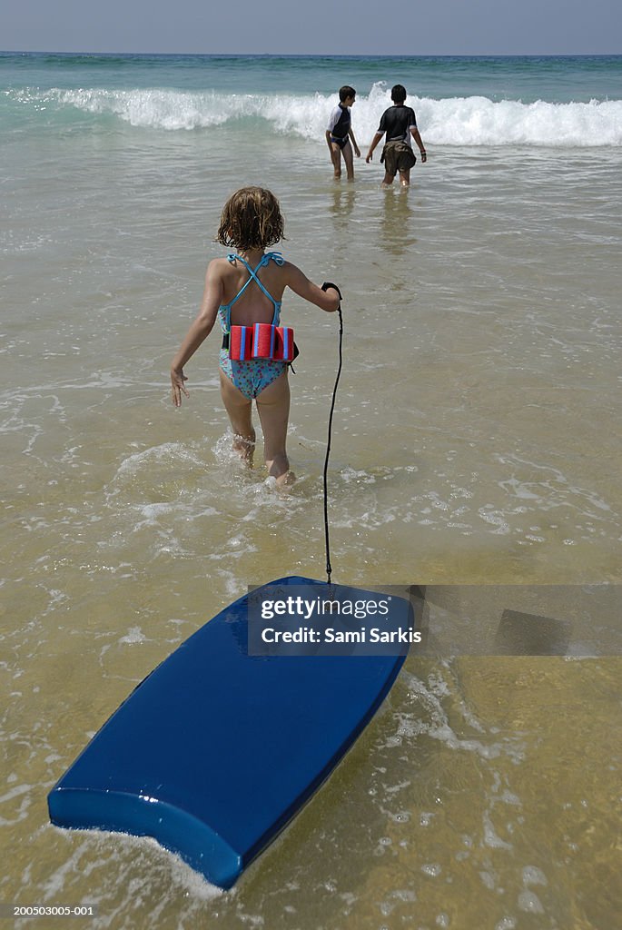 Girl (5-7) walking into surf, pulling float, rear view