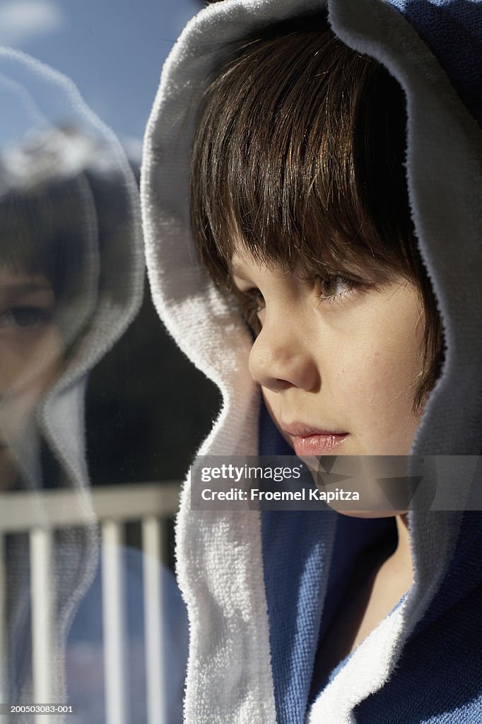 Boy (4-5 years) in bathrobe looking through window