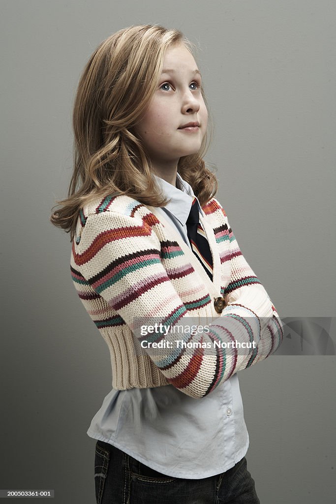 Girl (8-10) standing with arms crossed, looking up, side view