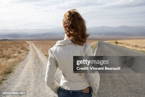 Young woman standing by two roads, outdoors, rear view Young woman standing by two roads, outdoors, rear view