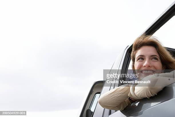 young woman leaning on car window smiling, close-up, low angle view - vincent young stock pictures, royalty-free photos & images