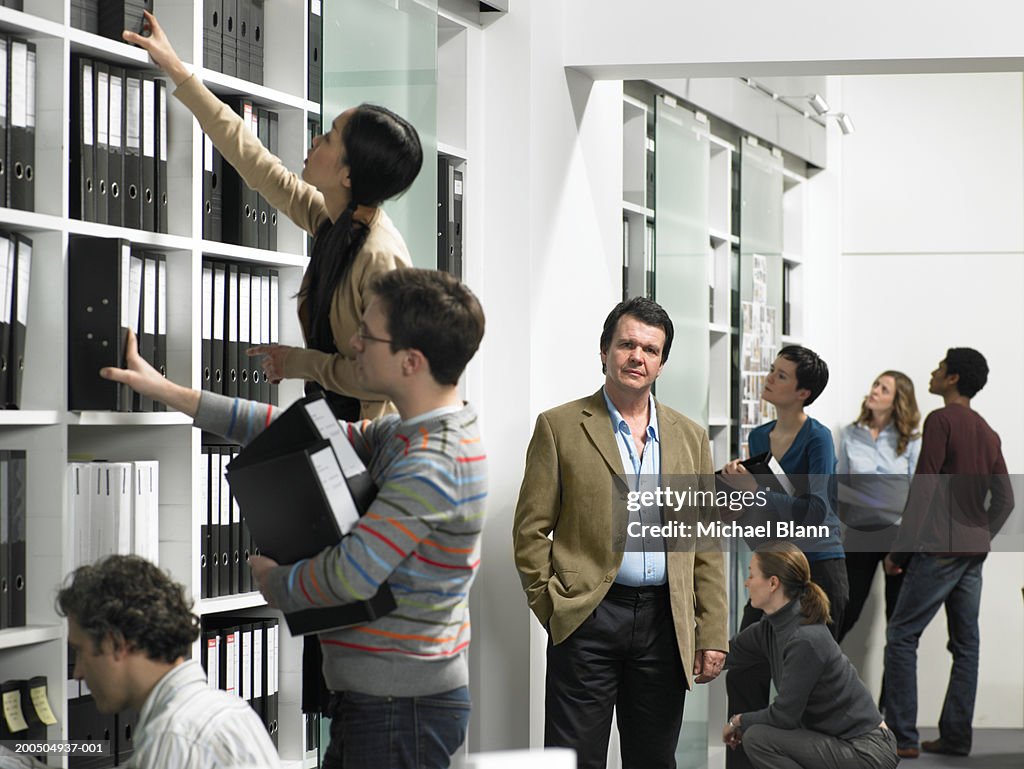 Business colleagues looking at folders on shelf in office, man smiling