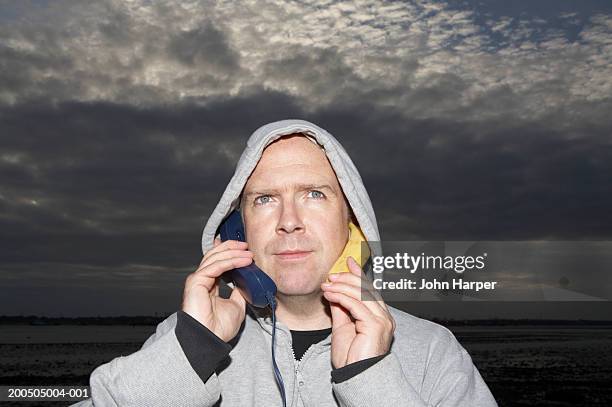 man using telephone and banana as phone by sea, close-up, dusk - banana phone stock pictures, royalty-free photos & images