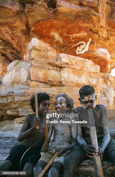 three aboriginal boys (10-14) playing didgeridoo and clapsticks - aboriginal kids outdoors nt stock pictures, royalty-free photos & images