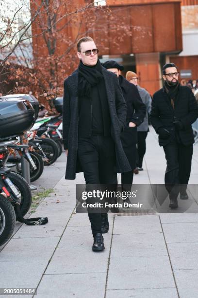 Guest wears Chester long coat, black skinny denim pants, black turtleneck sweater with black scarf outside Zegna show during the Milan Fashion Week -...