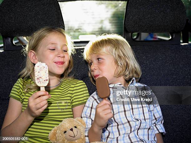 Brother and sister (4-7) sitting in car, eating ice cream, smiling