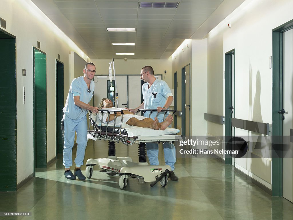 Two male nurses by patient on bed walk in hospital