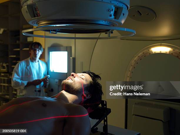 mature doctor by male patient lying on radiology bed - radiotherapy stock pictures, royalty-free photos & images
