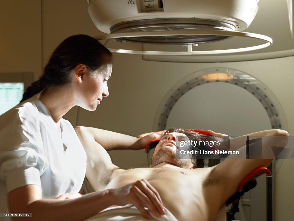 Female doctor by male patient lying under radiology machine