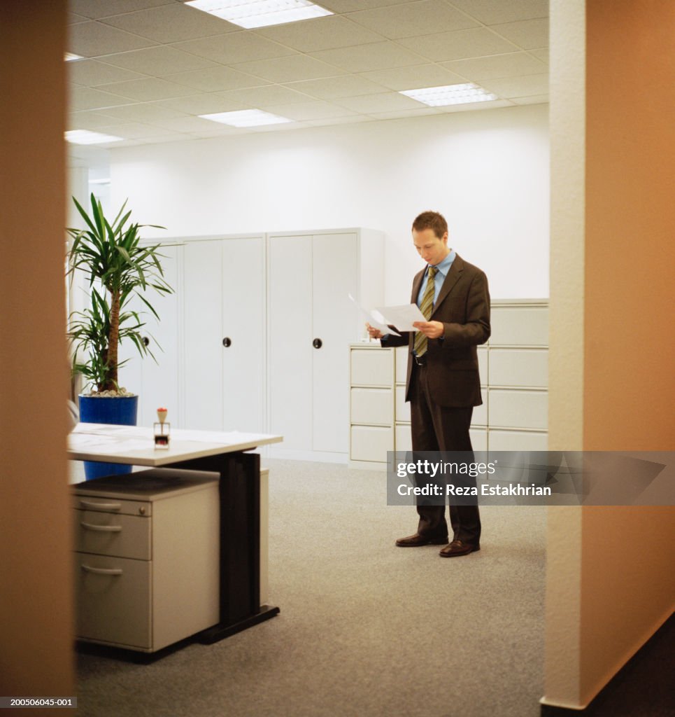 Businessman standing in center of office looking over paperwork