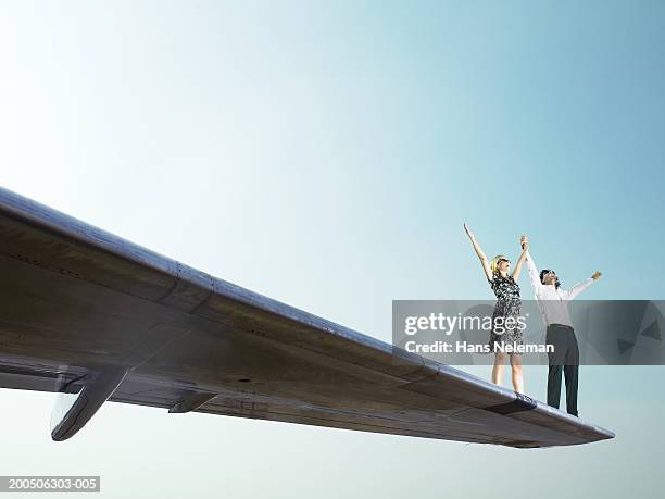 young couple standing on wing of airplane, arms outstretched - aircraft wing stock pictures, royalty-free photos & images