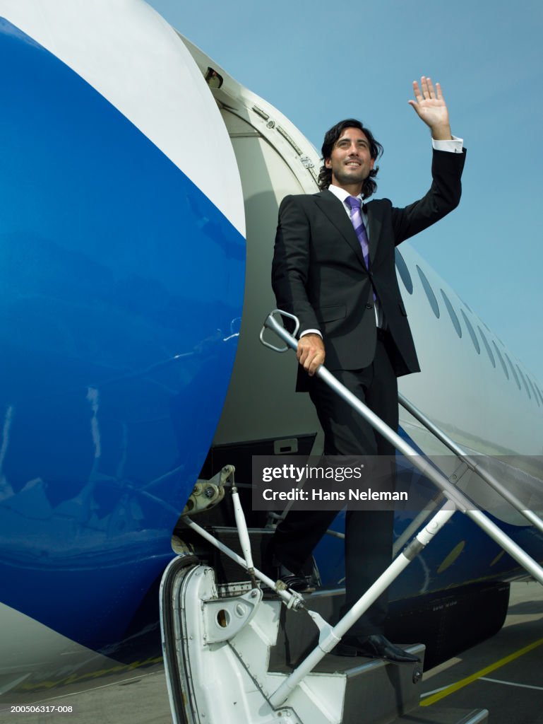 Young businessman getting off airplane, waving, smiling