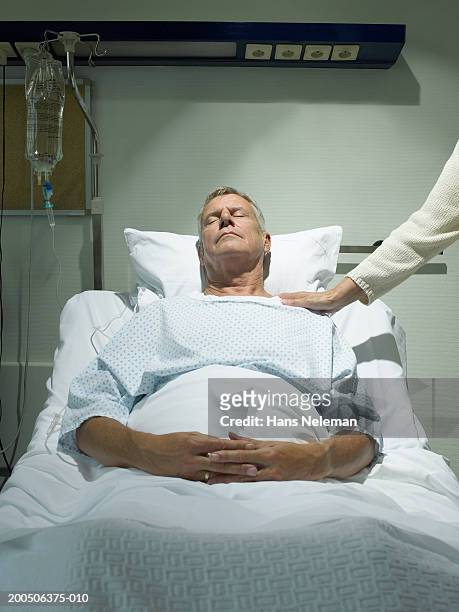 senior woman by senior man lying asleep in hospital bed - iv drip womans hand stock-fotos und bilder