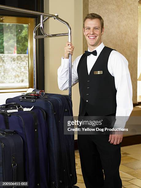 young man with luggage rack in hotel lobby, smiling, portrait - luggage rack stock pictures, royalty-free photos & images