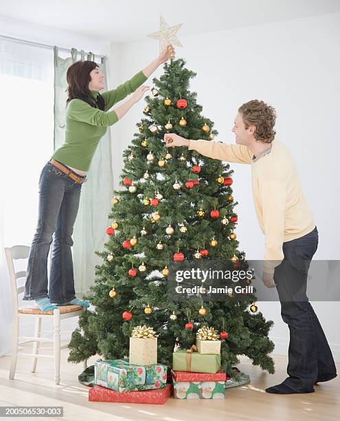 young couple decorating christmas tree - decorare l'albero di natale foto e immagini stock