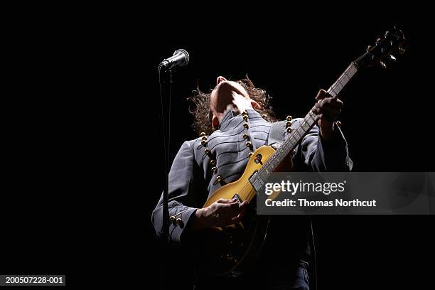 young man playing electric guitar on dark stage, head back - saiteninstrument stock-fotos und bilder