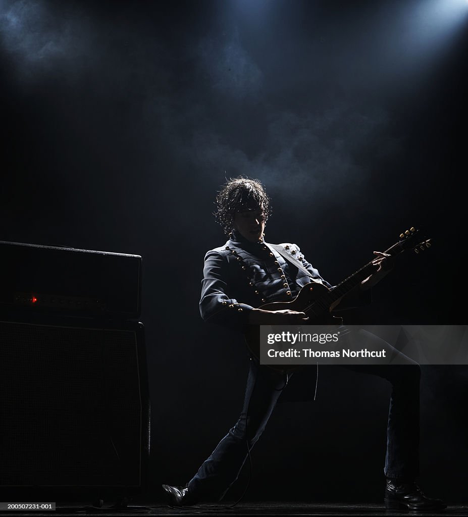 Young man playing electric guitar on dark stage