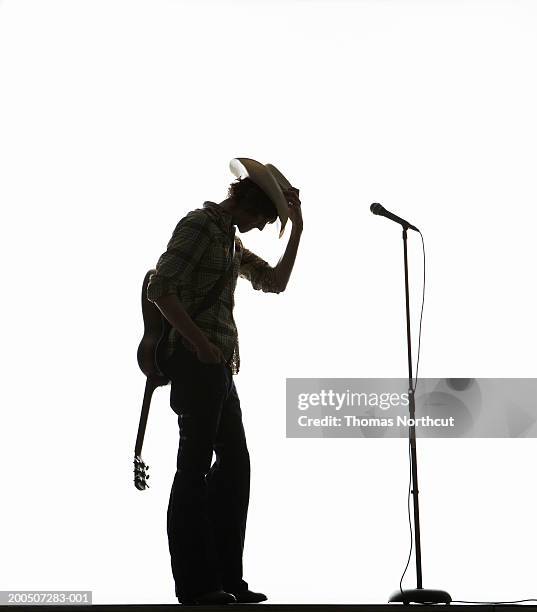 young man with acoustic guitar adjusting cowboy hat, side view - acoustic guitar white background stock pictures, royalty-free photos & images