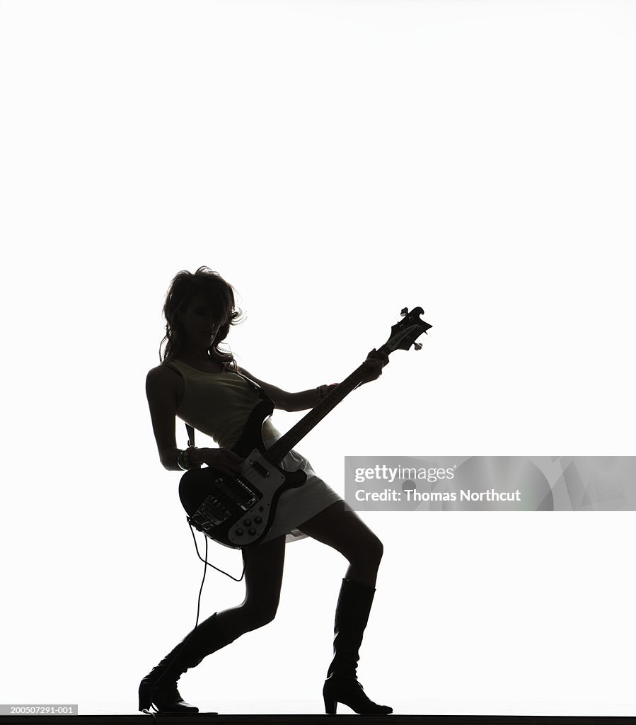 Silhouette of young woman playing bass guitar