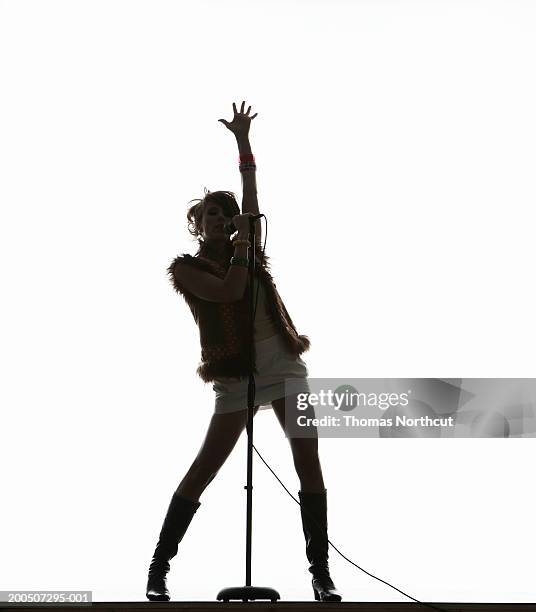 silhouette of young woman singing into microphone, arm raised - contraluz fotografías e imágenes de stock