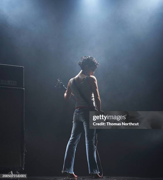 young woman playing bass guitar on smoky stage, rear view - bass gitarre stock-fotos und bilder