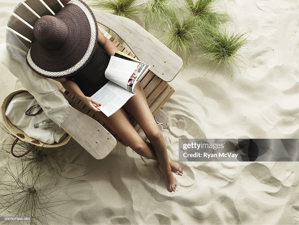 Young woman reading magazine on Adirondack chair, overhead view
