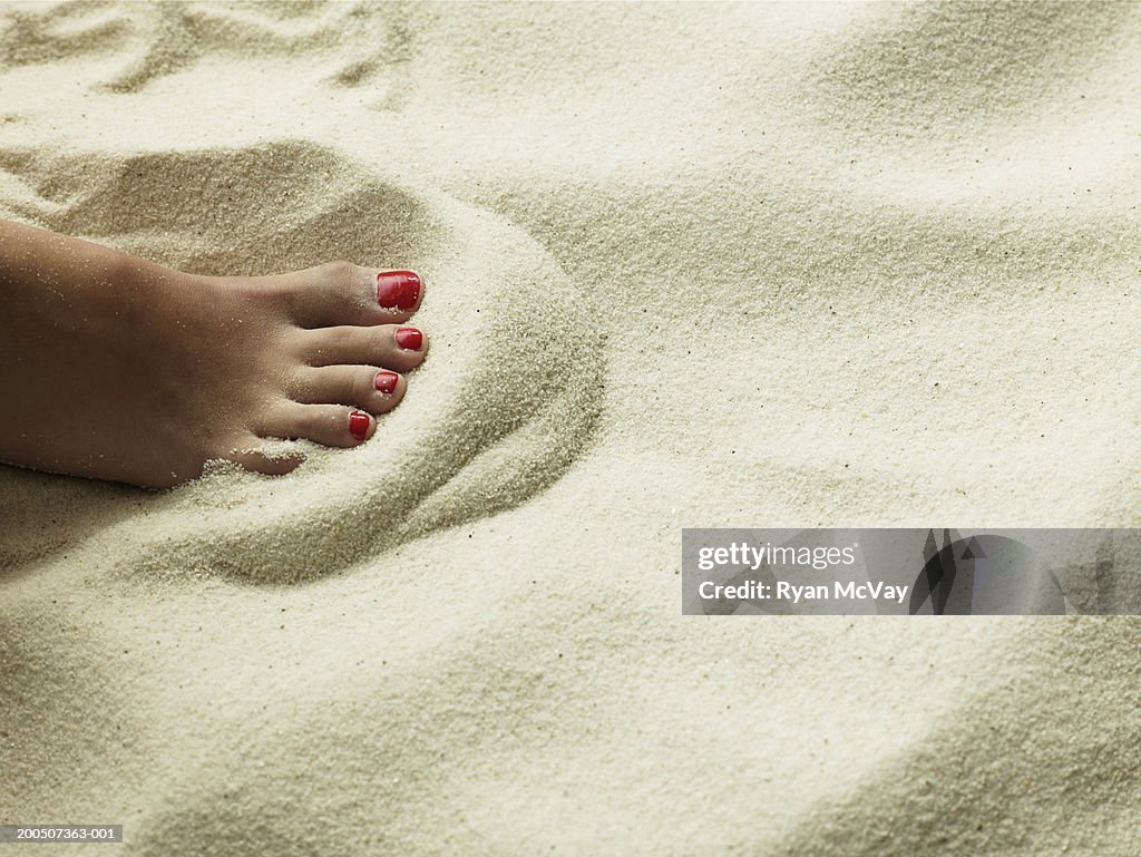 Young woman sitting on sand, close-up of foot