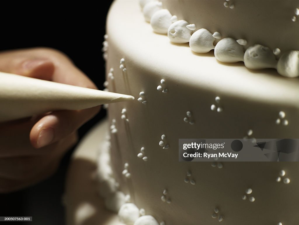 Woman decorating layered cake with icing bag, close-up of cake