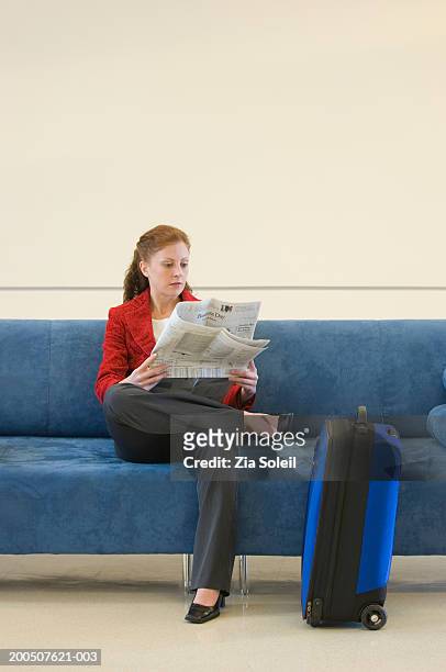 young woman reading newspaper by luggage on sofa - valise soleil stock pictures, royalty-free photos & images
