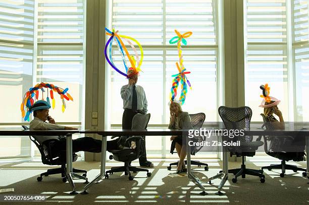four business people wearing balloon hats in meeting room - bizarre office stock pictures, royalty-free photos & images