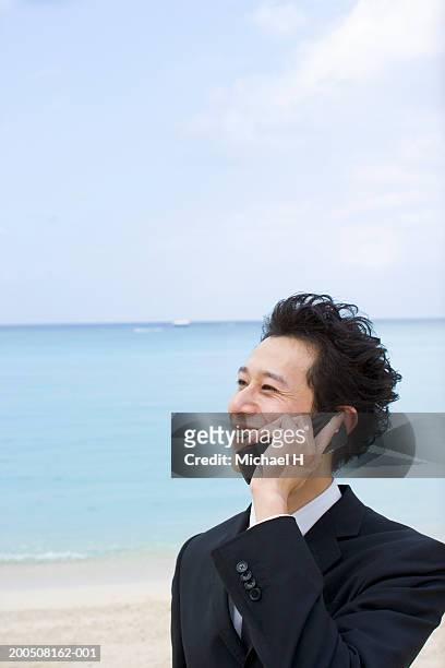 young businessman talking on cell phone on beach, smiling - black hair stock pictures, royalty-free photos & images