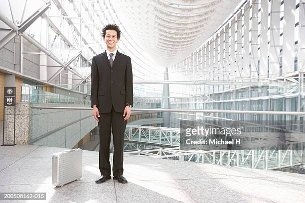 young businessman standing in corridor, smiling, portrait - ビジネスフォーマル ストックフォトと画像
