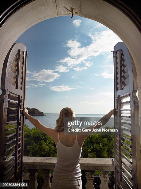 montenegro, sveti stefan, woman opening shutters, rear view - norman window fotografías e imágenes de stock