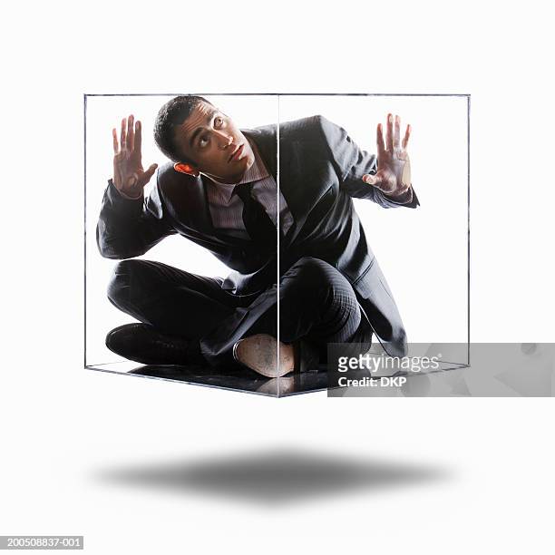 young businessman trapped inside transparent box, looking up - acorralado fotografías e imágenes de stock