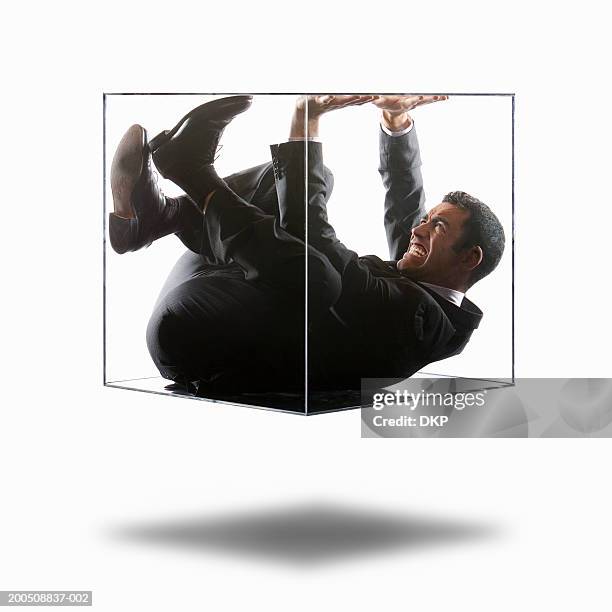 young businessman trying to push his way out of transparent box - confinement stock-fotos und bilder