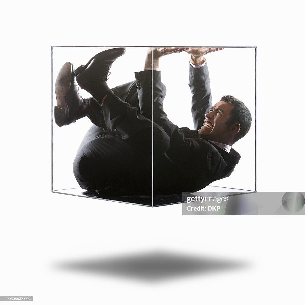 Young businessman trying to push his way out of transparent box
