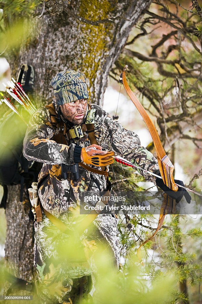 Male bow hunter wearing camouflage clothes standing by tree