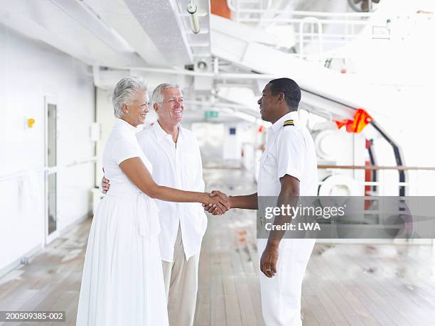 captain shaking hands with mature couple on deck of cruise ship - bootskapitän stock-fotos und bilder