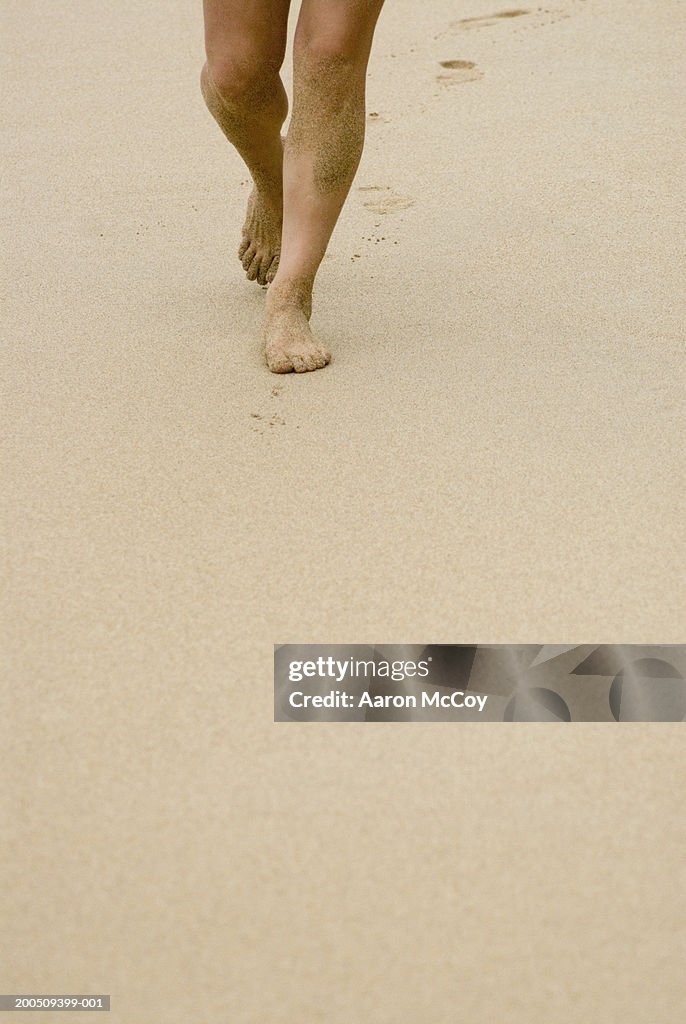 Woman walking along sandy beach, low section