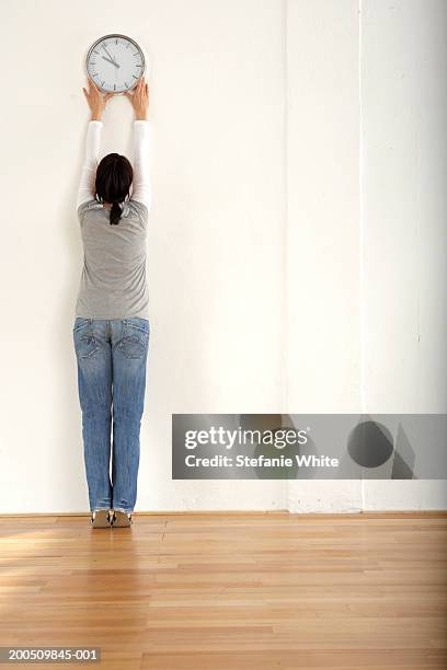 woman hanging clock on wall, rear view - hanging photos stock pictures, royalty-free photos & images