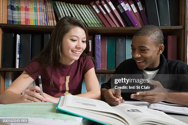 teenage boy and girl (12-14) studying in library, smiling - boy and girl talking fotografías e imágenes de stock