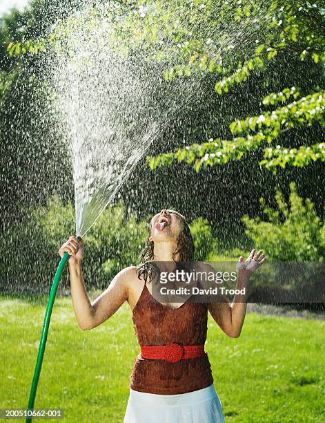 young woman spraying water from hose in garden - wet hose ストックフォトと画像