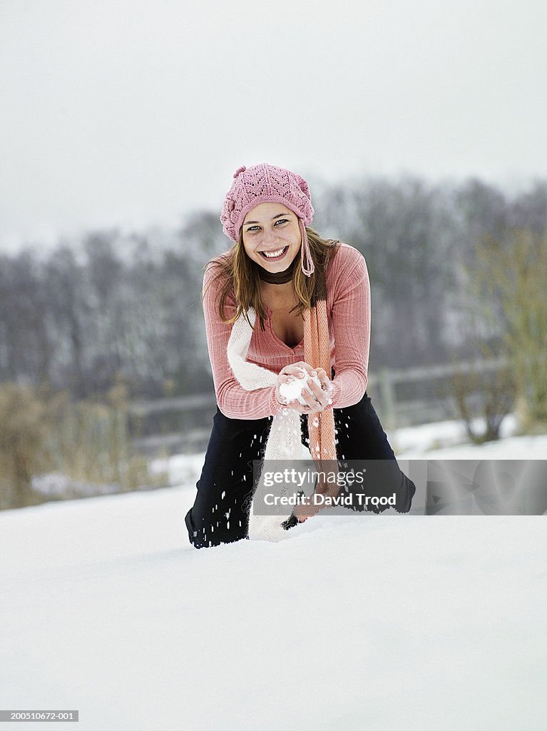 Young woman making snowball, kneeling on snow
