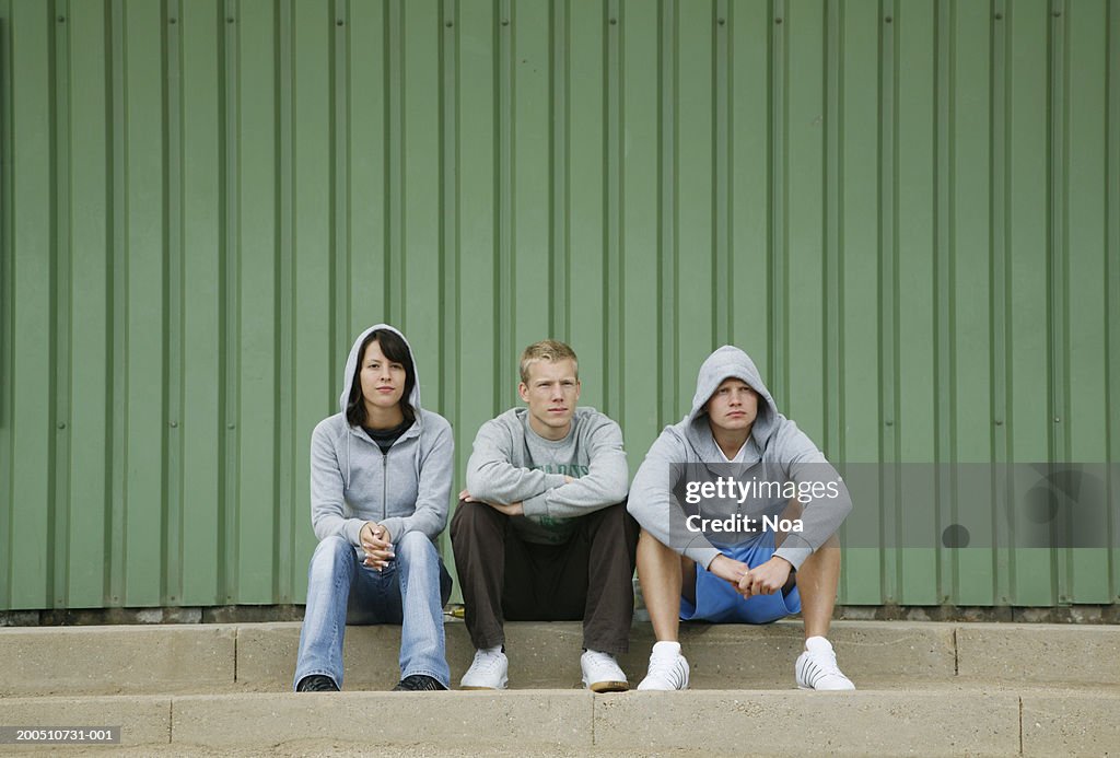 Three young adults sitting on steps in front of building