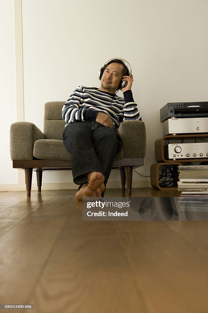 Mature man relaxing in armchair at home, listening to music