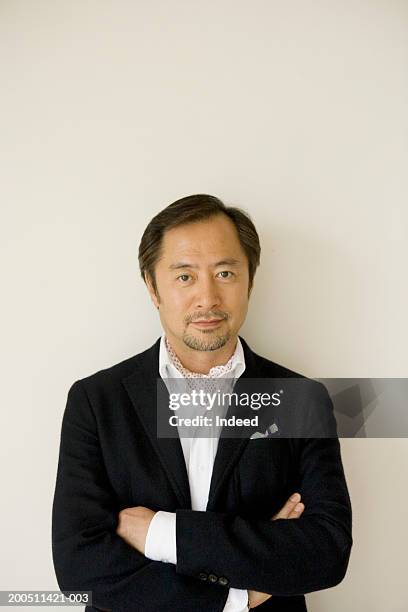 mature man standing against wall, arms folded, smiling, front view - 中年の男性一人 ストックフォトと画像