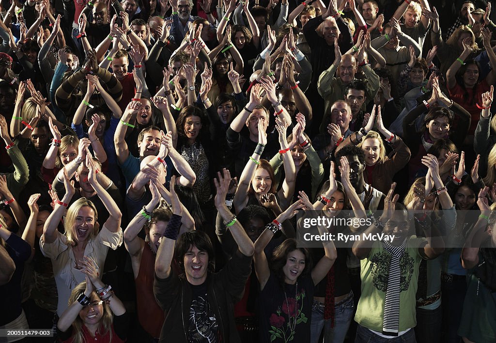 Audience at concert, clapping hands over heads, smiling, overhead view