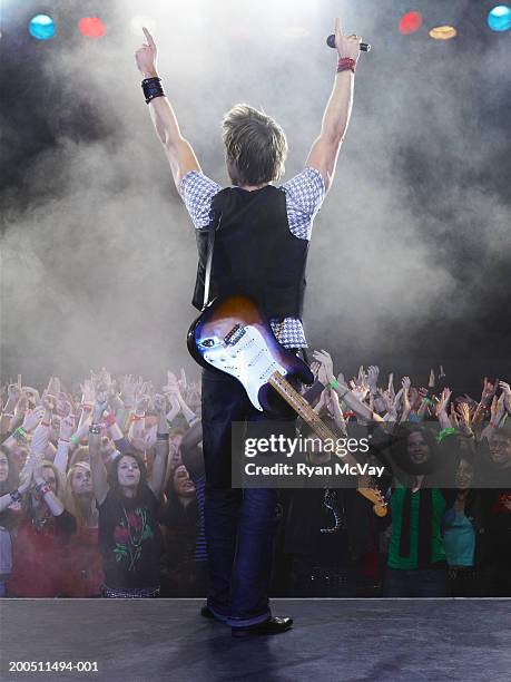 young male guitarist standing in front of audience, arms raised - boygroup stock-fotos und bilder