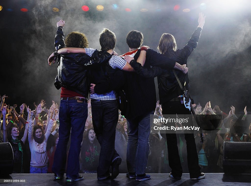 Band standing before audience on stage with arms around each other